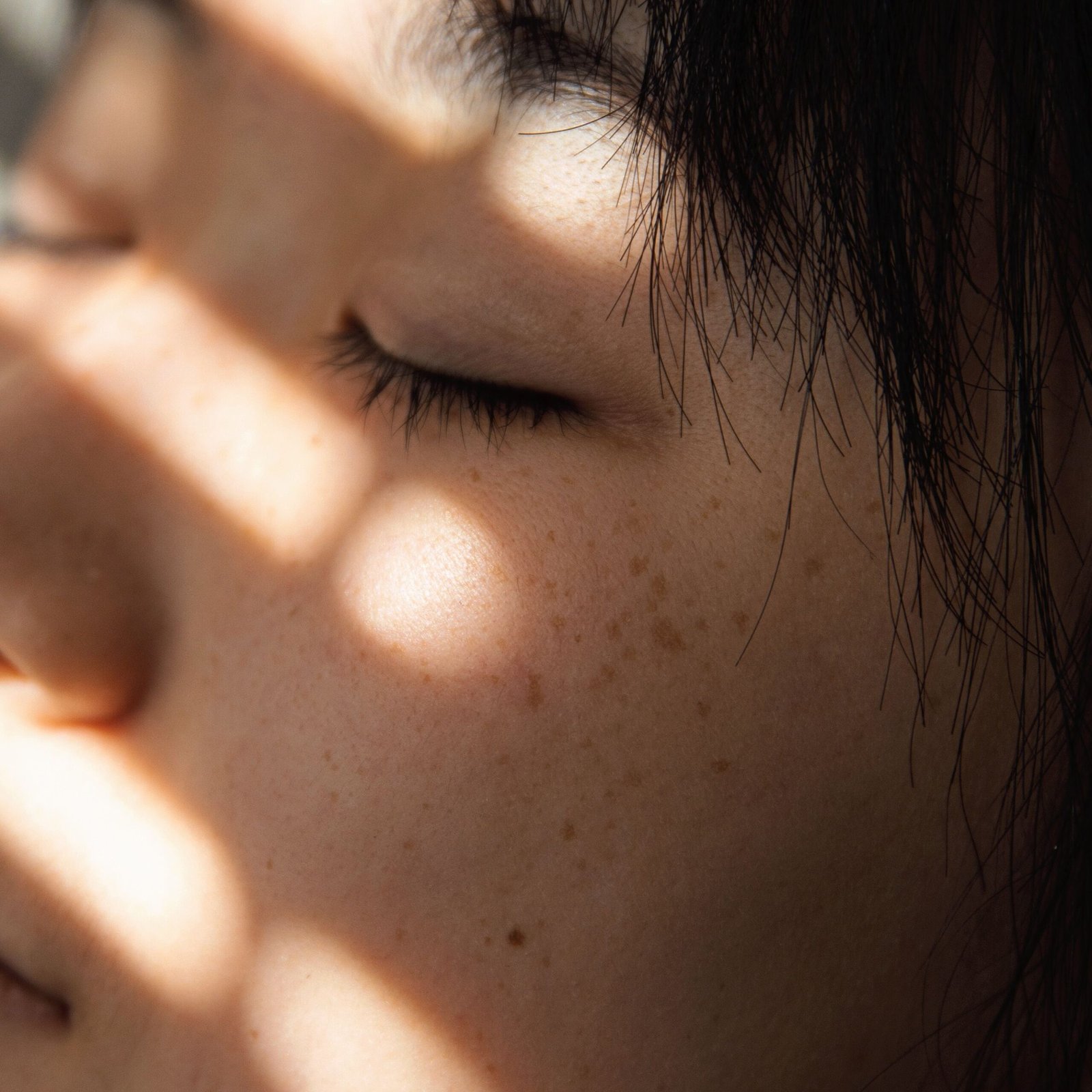 Close-up of an Asian woman with closed eyes, sunlight casting shadows.