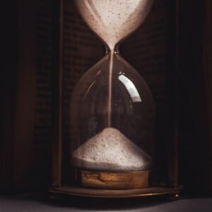 A close-up view of a vintage hourglass with sand running through it in a moody, dark setting.